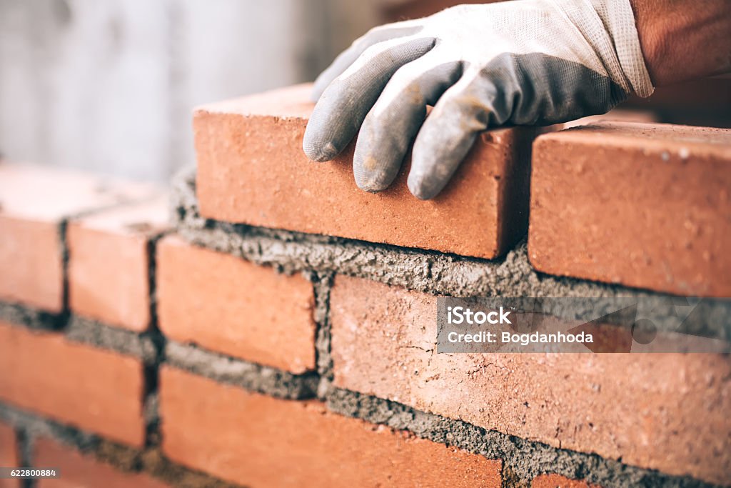 Home close up of industrial bricklayer installing bricks on construction site